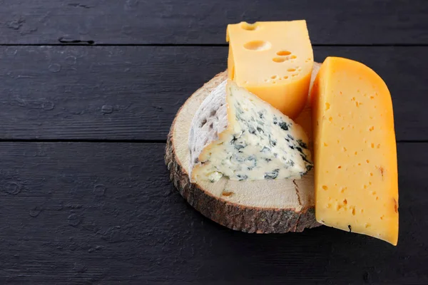 Sert peynir ve mavi peynir ahşap stand. Peynir siyah kurullarında farklı türleri. İsviçre peyniri ve dorblu koyu arka plan üzerinde