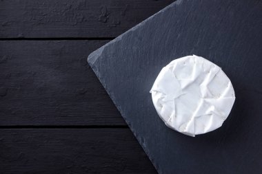 Camembert siyah taş gemide. Yumuşak peynir kalıp siyah arka plan ile. Minimalizm tarzı kayrak yazı tahtası üzerinde peynir. Kopya alanı