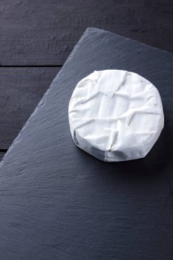 Camembert siyah taş gemide. Yumuşak peynir kalıp siyah arka plan ile. Minimalizm tarzı kayrak yazı tahtası üzerinde peynir. Kopya alanı
