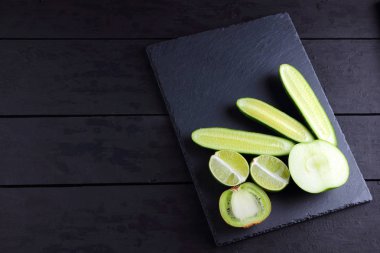 Yeşil meyveler, sebzeler kopya alanı siyah bir zemin üzerine. Doğal yeşil ürünler yaratıcı figürü. Salatalık, kivi, limon ve kayrak bir tahta üzerinde yeşil elma