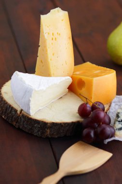 Peynir, armut ve ahşap tahta üzerinde üzüm türleri. Dilim çeşitli peynirler ve üzüm üzerinde arka plan bulanık. Dorblu, camembert ve parşömen kağıt üzerine sert sarı peynir