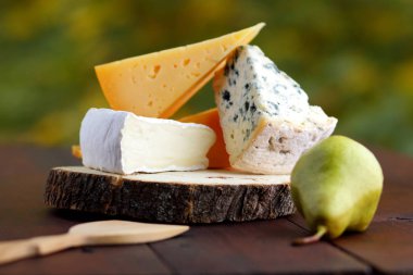 Peynir ve armut ahşap kurullarında çeşitli türleri. Dilim peynir üzerinde arka plan bulanık. Dorblu, camembert ve sert sarı peynir