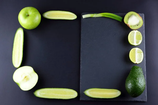 Green fruits and vegetables on black background with creative copy space. Frame from natural products green. Avocado, kiwi, lime and apple on slate board. Top view