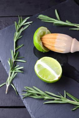 Kireç yarısı ve kayrak tahta üzerinde ahşap meyve sıkacağı. Limon ve biberiye siyah arka plan üzerine. Taze limon suyu taş Pano akar. Sağlıklı gıda