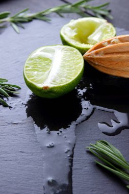 Kireç yarısı ve kayrak tahta üzerinde ahşap meyve sıkacağı. Limon ve biberiye siyah arka plan üzerine. Taze limon suyu taş Pano akar. Sağlıklı gıda