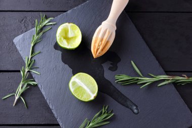 Kireç yarısı ve kayrak tahta üzerinde ahşap meyve sıkacağı. Limon ve biberiye siyah arka plan üzerine. Taze limon suyu taş Pano akar. Sağlıklı gıda