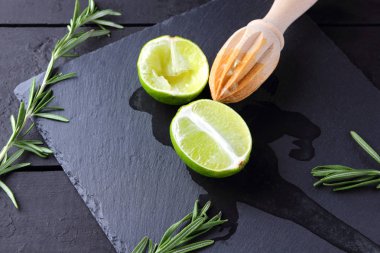 Kireç yarısı ve kayrak tahta üzerinde ahşap meyve sıkacağı. Limon ve biberiye siyah arka plan üzerine. Taze limon suyu taş Pano akar. Sağlıklı gıda
