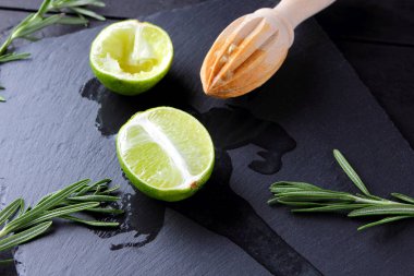 Kireç yarısı ve kayrak tahta üzerinde ahşap meyve sıkacağı. Limon ve biberiye siyah arka plan üzerine. Taze limon suyu taş Pano akar. Sağlıklı gıda