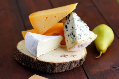 Peynir ve armut ahşap kurullarında çeşitli türleri. Dilim peynir üzerinde arka plan bulanık. Dorblu, camembert ve sert sarı peynir