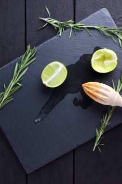Kireç yarısı ve kayrak tahta üzerinde ahşap meyve sıkacağı. Limon ve biberiye siyah arka plan üzerine. Taze limon suyu taş Pano akar. Sağlıklı gıda