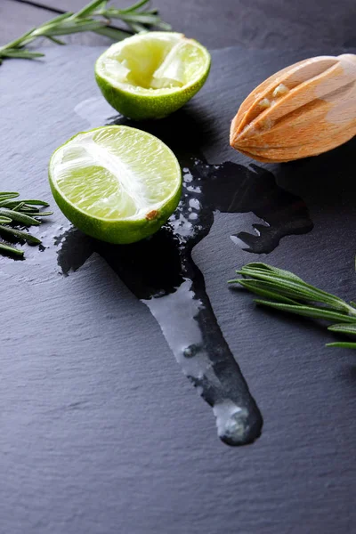 Kireç yarısı ve kayrak tahta üzerinde ahşap meyve sıkacağı. Limon ve biberiye siyah arka plan üzerine. Taze limon suyu taş Pano akar. Sağlıklı gıda