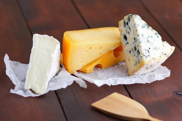 木板上的奶酪 各种奶酪在自然模糊的背景 羊皮纸上的多布布 卡门伯特和硬黄色奶酪 复制空间 — 图库照片