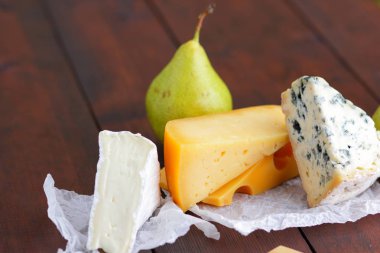 Peynir ve armut ahşap kurullarında. Çeşitli peynir üzerinde doğal arka plan bulanık. Dorblu, camembert ve parşömen kağıt üzerine sert sarı peynir