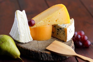 Peynir, armut ve üzüm ahşap kurullarında. Çeşitli türde peynir ve meyve üzerinde arka plan bulanık. Dorblu, camembert ve sert sarı peynir