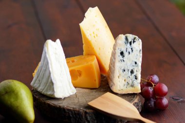Peynir, armut ve üzüm ahşap kurullarında. Çeşitli türde peynir ve meyve üzerinde arka plan bulanık. Dorblu, camembert ve sert sarı peynir
