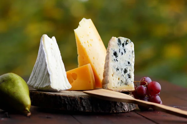 木板上的奶酪 梨和葡萄 不同类型的奶酪和水果在模糊的背景 多布卢 卡门伯特和硬黄色奶酪 — 图库照片