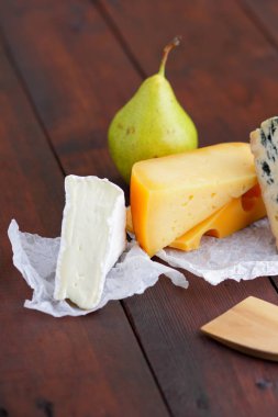 Peynir ve armut ahşap kurullarında. Çeşitli peynir üzerinde doğal arka plan bulanık. Dorblu, camembert ve parşömen kağıt üzerine sert sarı peynir