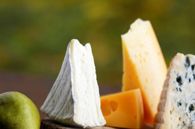 Peynir ve armut ahşap kurullarında. Çeşitli peynir üzerinde doğal arka plan bulanık. Dorblu, camembert ve parşömen kağıt üzerine sert sarı peynir