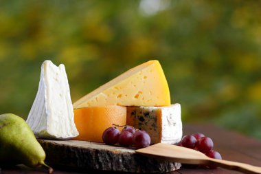 Peynir, armut ve üzüm ahşap kurullarında. Çeşitli türde peynir ve meyve üzerinde arka plan bulanık. Dorblu, camembert ve sert sarı peynir