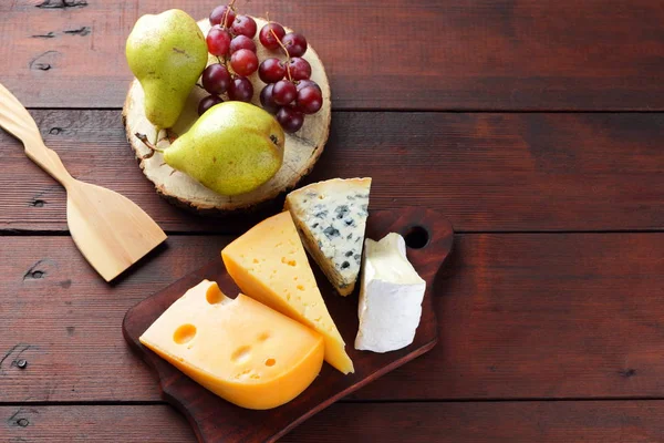 Peynir, armut ve ahşap kurullarında üzüm türleri. Peynir ve meyve ahşap arka plan üzerinde. Dorblu, camembert ve sert sarı peynir. Üstten Görünüm