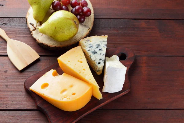 Peynir, armut ve ahşap kurullarında üzüm türleri. Peynir ve meyve ahşap arka plan üzerinde. Dorblu, camembert ve sert sarı peynir. Üstten Görünüm