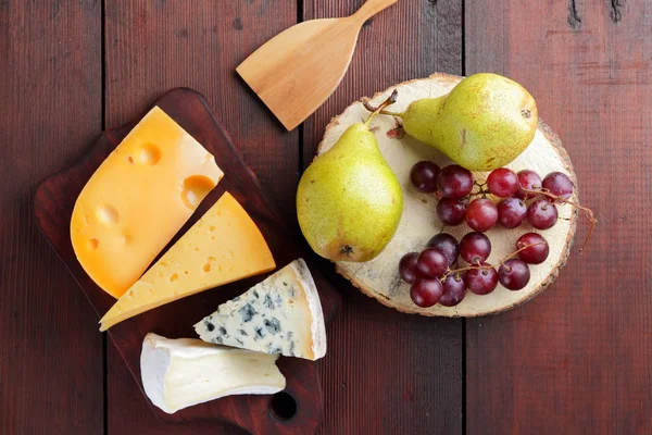 Peynir, armut ve ahşap kurullarında üzüm türleri. Peynir ve meyve ahşap arka plan üzerinde. Dorblu, camembert ve sert sarı peynir. Üstten Görünüm
