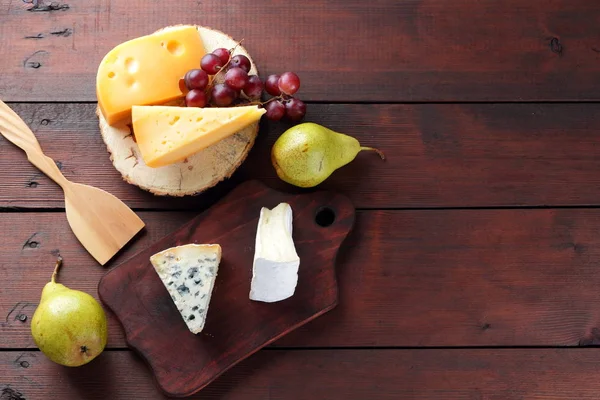 Various types of cheese, pears and grapes on wooden boards. Cheese and fruits on wooden background. Dorblu, camembert and hard yellow cheese. Top view