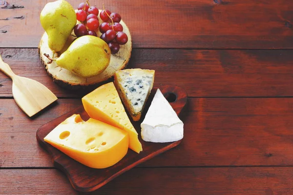 Various types of cheese, pears and grapes on wooden boards. Cheese and fruits on wooden background. Dorblu, camembert and hard yellow cheese. Top view
