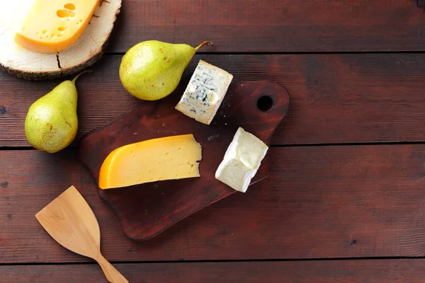 Various types of cheese and pears on wooden boards. Cheese and fruits on wooden background. Dorblu, camembert and hard yellow cheese. Top view