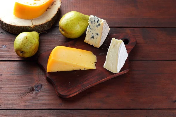 Various types of cheese and pears on wooden boards. Cheese and fruits on wooden background. Dorblu, camembert and hard yellow cheese. Top view