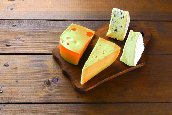 Cheese on wooden boards. Various types of cheese on wooden background. Dorblu, camembert and hard yellow cheese. Top view