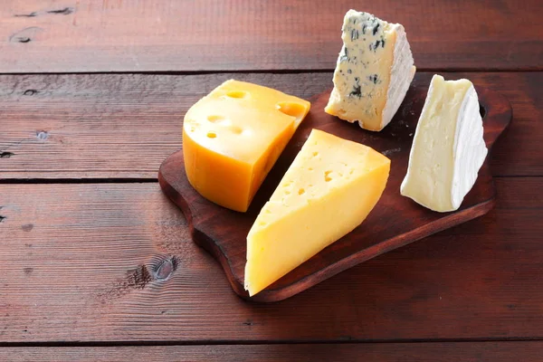 Cheese on wooden boards. Various types of cheese on wooden background. Dorblu, camembert and hard yellow cheese. Top view