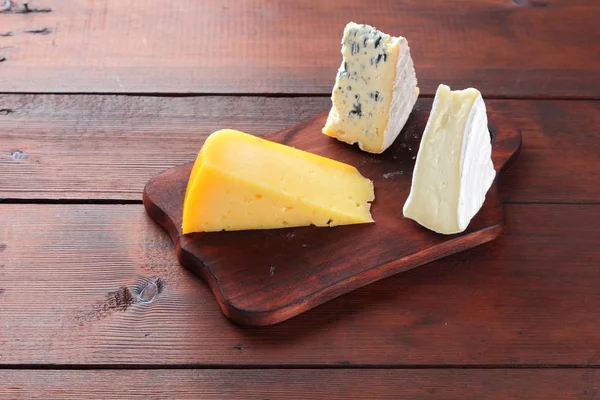 Cheese on wooden boards. Various types of cheese on wooden background. Dorblu, camembert and hard yellow cheese. Top view
