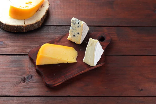 Peynir ahşap kurullarında. Ahşap arka plan üzerinde peynir türleri. Dorblu, camembert ve sert sarı peynir. Üstten Görünüm