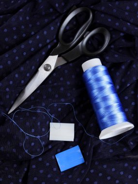 Koyu kumaş lekeli ve mavi İpek iplik ile. Terzilik işlemi. Makas ve bobin iplik siyah kumaş üzerine. Parlak mavi konu dikiş için. Üstten Görünüm