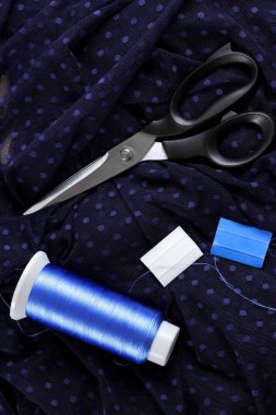 Koyu kumaş lekeli ve mavi İpek iplik ile. Terzilik işlemi. Makas ve bobin iplik siyah kumaş üzerine. Parlak mavi konu dikiş için. Üstten Görünüm