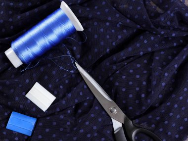 Koyu kumaş lekeli ve mavi İpek iplik ile. Terzilik işlemi. Makas ve bobin iplik siyah kumaş üzerine. Parlak mavi konu dikiş için. Üstten Görünüm