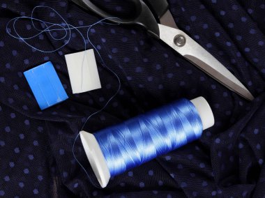 Koyu kumaş lekeli ve mavi İpek iplik ile. Terzilik işlemi. Makas ve bobin iplik siyah kumaş üzerine. Parlak mavi konu dikiş için. Üstten Görünüm