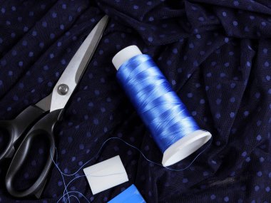 Koyu kumaş lekeli ve mavi İpek iplik ile. Terzilik işlemi. Makas ve bobin iplik siyah kumaş üzerine. Parlak mavi konu dikiş için. Üstten Görünüm