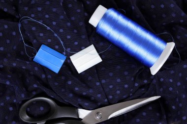 Koyu kumaş lekeli ve mavi İpek iplik ile. Terzilik işlemi. Makas ve bobin iplik siyah kumaş üzerine. Parlak mavi konu dikiş için. Üstten Görünüm