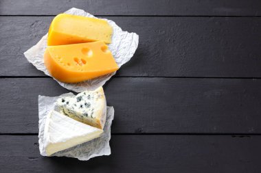 Sert sarı peynir, camembert ve mavi peynir siyah kurullarında. Parşömen kağıt üzerine peynir türleri. İsviçre peyniri ve dorblu koyu arka plan üzerinde. Üstten Görünüm