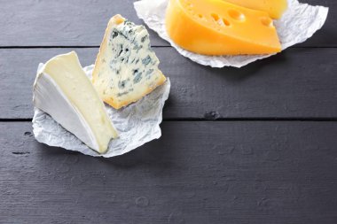 Sert sarı peynir, camembert ve mavi peynir siyah kurullarında. Parşömen kağıt üzerine peynir türleri. İsviçre peyniri ve dorblu koyu arka plan üzerinde. Üstten Görünüm