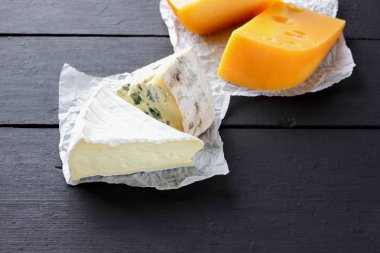 Sert sarı peynir, camembert ve mavi peynir siyah kurullarında. Parşömen kağıt üzerine peynir türleri. İsviçre peyniri ve dorblu koyu arka plan üzerinde. Üstten Görünüm