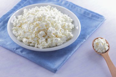 Mavi peçete üzerinde süzme peynir. Tahta kaşık ile beyaz plaka üzerinde süzme peynir. Yumuşak peynir diyet için. Kahvaltı için sağlıklı süt ürünleri