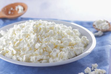 Mavi peçete üzerinde süzme peynir. Tahta kaşık ile beyaz plaka üzerinde süzme peynir. Yumuşak peynir diyet için. Kahvaltı için sağlıklı süt ürünleri