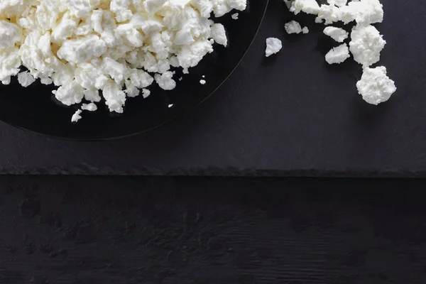 Cottage cheese on black slate board. Cottage cheese on black plate. Soft cheese for diet on black boards. Healthy dairy product for breakfast. Concept