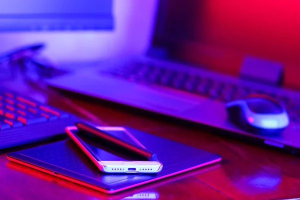 Workplace digital designer. Freelancer workplace in neon light. Computer, graphics tablet and smartphone on the table. Place for creativity in blue-pink light