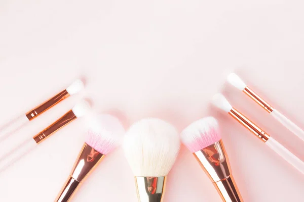 Makeup brushes on pink background. Set of golden makeup brushes, concept. Woman beauty accessory in pastel colors. Copy space. Flat lay