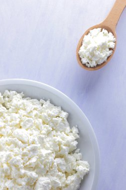 Tahta kaşık ile beyaz plaka üzerinde süzme peynir. Beyaz arka plan üzerinde süzme peynir. Yumuşak peynir diyet için. Kahvaltı için sağlıklı süt ürünleri