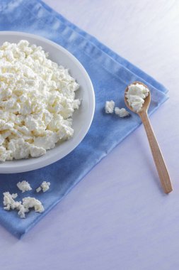 Mavi peçete üzerinde süzme peynir. Peynir tahta kaşıkla beyaz tabakta. Yumuşak peynir diyet için. Kahvaltı için sağlıklı süt ürünleri